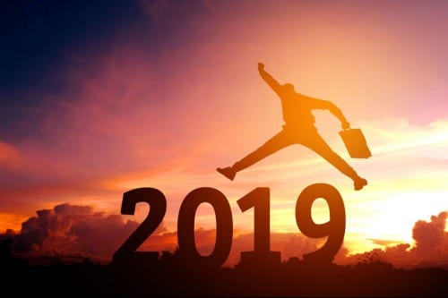 A person jumping over large block numbers spelling out 2019 with a sunset behind them