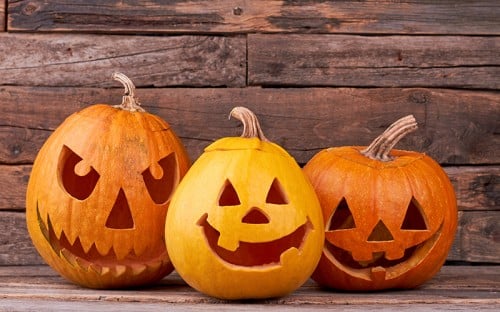 Three orange pumpkins with carved smiling faces against a wooden background
