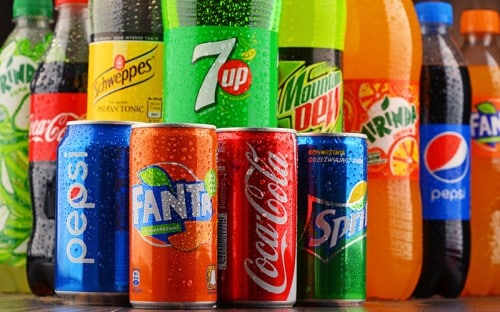 Multiple cans of colorful soda options in front of large bottles of soda